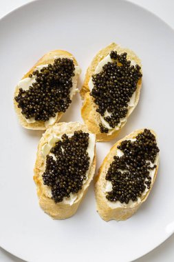 Siyah havyarlı baget dilimleri ve beyaz tabakta tereyağı. Doğal mersin balıklı, lüks, lezzetli bir sandviç. Deniz ürünleri ve ekmek aperatifi..