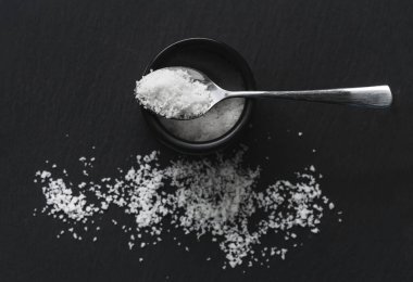 Organik deniz tuzu, kavanoz ve siyah taştan bir arka planda kaşık. Doğal sağlıklı yemek pişirme kavramı.