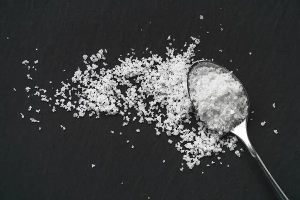 黒スレートの石の背景に有機海の白い塩とスプーン 天然の健康食品の調理の概念 — ストック写真