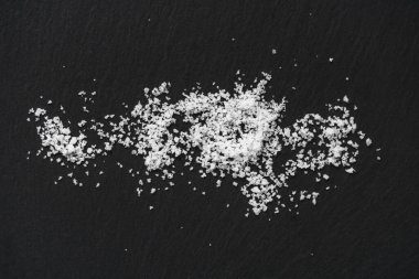 Siyah bir taş zemin üzerinde organik deniz beyaz tuzu yığını. Doğal sağlıklı yemek pişirme kavramı.