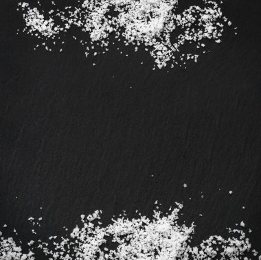 Sprinkled organic sea white salt on a black slate stone background. Concept of cooking natural healthy food. Copy space. 
