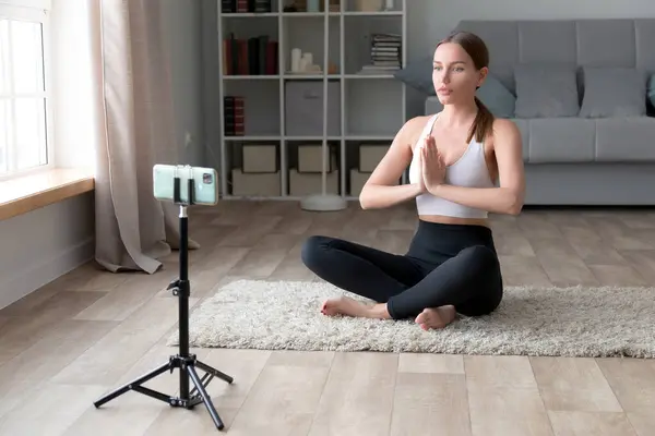 漂亮的年轻女子穿着运动服在家里做瑜伽 Fitness博客为她的博客录影 图库图片