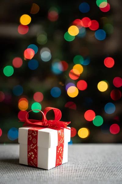 クリスマスツリーの背景の前に赤いリボンの白いギフトボックス — ストック写真