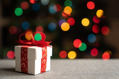 Kırmızı kurdeleli beyaz hediye kutusu Noel ağacı arka planında