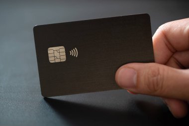 Closeup of hand holding single credit card on black background