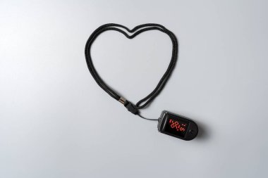 Close up of pulse oximeter device with strap arranged in heart shape on gray background