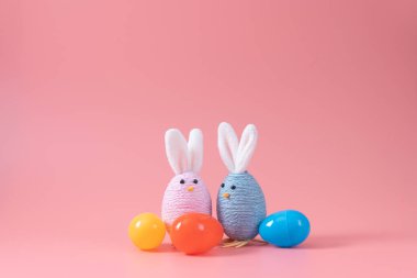 Pastel colored eggs and handmade easter bunny decorations lined up on pink background