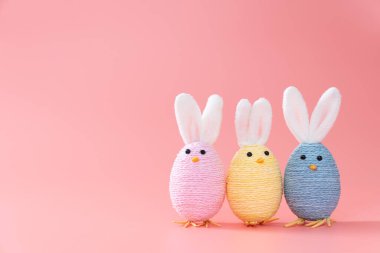 Pastel colored handmade easter bunny decorations lined up on pink background