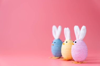 Pastel colored handmade easter bunny decorations lined up on pink background