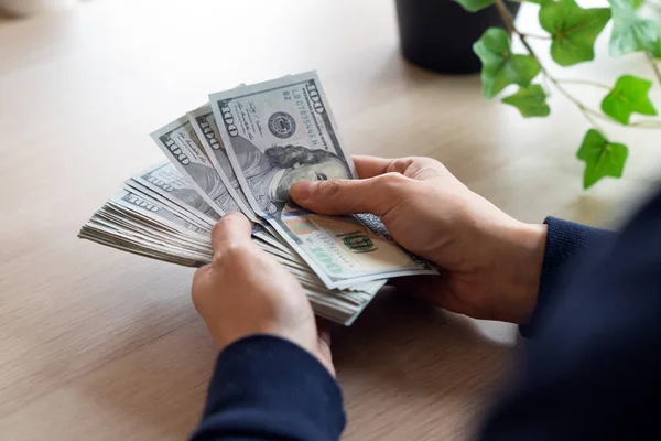 女性手在桌上清点堆积如山的100美元钞票的特写镜头 免版税图库图片