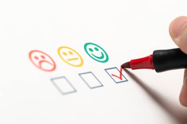 Happy customer checked mark tick on the smiley face icon on product quality and customer satisfaction survey and questionnaire checklist sheet with a red pen clipart