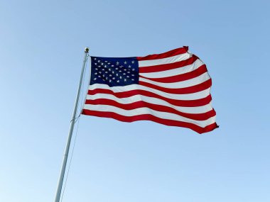 Rüzgarda dalgalanan Amerikan bayrağı, arka planda mavi bir gökyüzü, yer seviyesinden manzara.