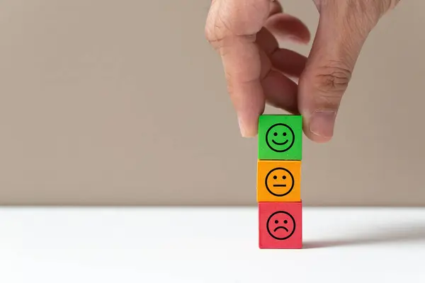 Customer service evaluation and satisfaction survey concepts. The happy user hand picked the happy smiley face icon on wooden cube block on white background.