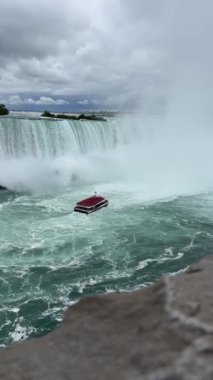 Kırmızı pançolu turistlerle dolu bir tur teknesi Niagara Şelalesi 'ndeki Horseshoe Şelalesi' nin tabanında sise doğru yol alıyor..