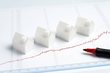 Beyaz model evler kırmızı kalemli grafik çizelgesine yerleştirilmiş. Çizelgede yükselen bir eğilim, emlak piyasası değerlerinin yükseliş veya fiyat artışına işaret ediyor.