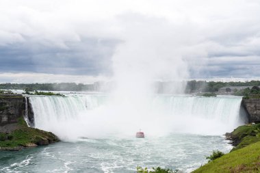 Kırmızı pançolu turistlerle dolu bir tur teknesi Niagara Şelalesi 'ndeki Horseshoe Şelalesi' nin tabanında sise doğru yol alıyor..