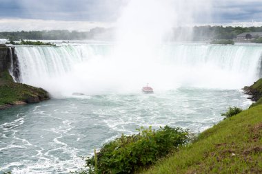 Kırmızı pançolu turistlerle dolu bir tur teknesi Niagara Şelalesi 'ndeki Horseshoe Şelalesi' nin tabanında sise doğru yol alıyor..