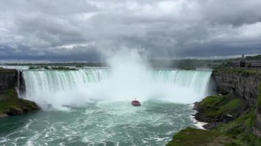 Kırmızı pançolu turistlerle dolu bir tur teknesi Niagara Şelalesi 'ndeki Horseshoe Şelalesi' nin tabanında sise doğru yol alıyor..