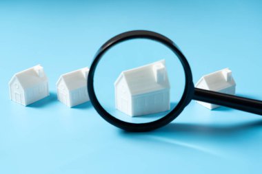 Büyüteç ev arama konsepti için mavi arka planda izole edilmiş bir ev modeline odaklanır