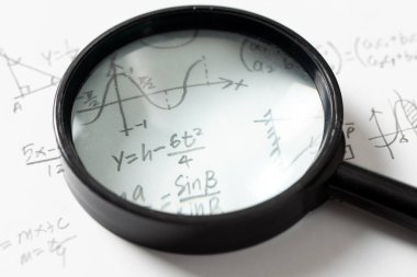 El yazısıyla yazılmış matematiksel denklemler, bir sinüs dalgası grafiği, geometrik şekiller ve büyüteçle beyaz kağıt üzerinde bir dik üçgen diyagramı.