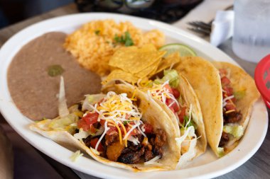 Baharatlı et, marul, domates ve peynirle dolu üç taco içeren lezzetli bir tabak Meksika mutfağı. Kızarmış fasulye ve pilav ile servis edilir.