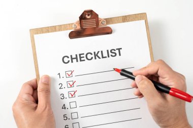 Tahta panodaki kontrol listesi, beyaz listedeki ögeleri işaretlemek için kırmızı işaret kalemi kullanan eller