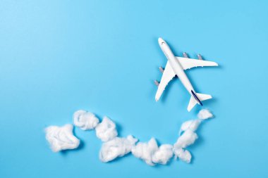 Gökyüzünde uçan minyatür bir model uçak mavi arkaplana karşı pamuk toplarından yapılmış bulutlarla basit bir seyahat veya tatil tasarımı için görsel olarak çarpıcı bir sahne yaratıyor.