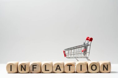 Tahta bloklar üzerinde minyatür bir alışveriş arabası olan INFLATION yazılıyor. Artan fiyatlar ve tüketici maliyetlerinin ekonomik etkisini simgeliyor..