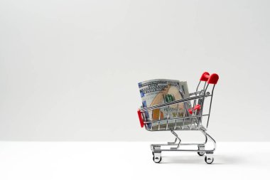 Beyaz arka plan, enflasyon veya bütçe kavramına izole edilmiş Amerikan doları banknotlarıyla dolu kırmızı minyatür alışveriş arabası