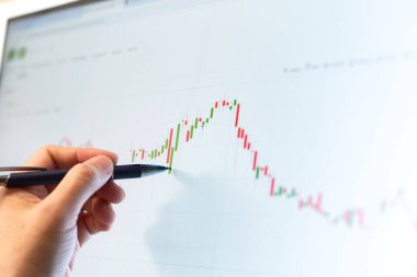 Borsa verilerini kontrol eden tüccarın eli, ekranda şamdanlar.