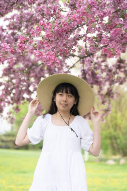İlkbaharda çekilmiş canlı pembe çiçeklerle kaplı bir ağacın altında gülümseyen beyaz elbiseli bir kızın portresi..