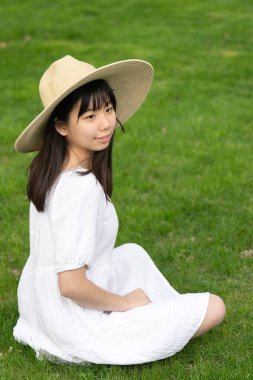 Genç bir kızın portresi açık havada gülümseyen bir şapka takıyor. Yumuşak, yeşil çimenli bir arka planı var..