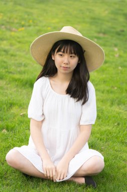 Genç bir kızın portresi açık havada gülümseyen bir şapka takıyor. Yumuşak, yeşil çimenli bir arka planı var..