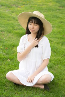 Genç bir kızın portresi açık havada gülümseyen bir şapka takıyor. Yumuşak, yeşil çimenli bir arka planı var..