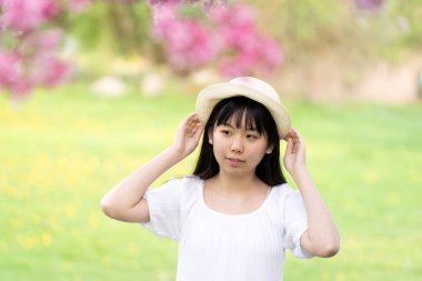 İlkbaharda çekilmiş canlı pembe çiçeklerle kaplı bir ağacın altında gülümseyen beyaz elbiseli bir kızın portresi..