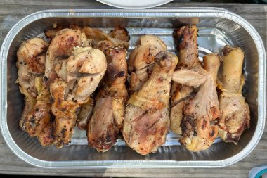 Bir tepsi baharatlı, ızgara tavuk budu, mükemmel pişmiş, altın-kahverengiyle kaplanmış, folyo kabında servis ediliyor..