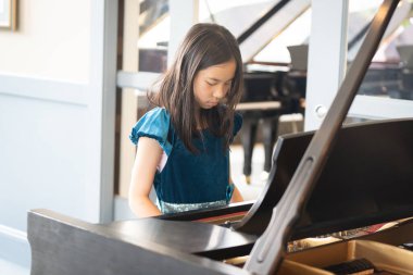 Işıldayan mavi elbiseli genç bir kız bir piyanonun başında zarif bir şekilde oturur, enstrüman çalar, parlak, zarif bir oda.