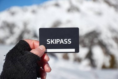 Ski pass held in hand by skier in a snowy mountain landscape clipart