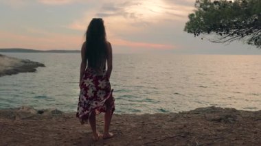 Deniz kıyısında sıcak yaz akşamının tadını çıkaran genç bir kadın, ağır çekimde esinti yapan etek.