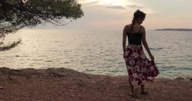 Deniz kıyısında sıcak yaz akşamının tadını çıkaran genç bir kadın, ağır çekimde esinti yapan etek.
