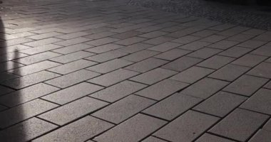 Sokaktan yavaş çekimde geçen insan figürlerinin gölgeli kaldırım taşları.