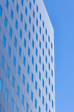 Şehirdeki mavi gökyüzünü yansıtan pencereli ofis binası detayı