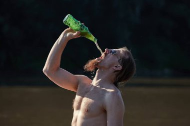 Kumsalda sakallı adam bira içiyor yukarıdan deli gibi bira döküyor.