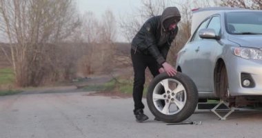 Arabanın tekerleği değişiyor, yol kenarında yedek lastik var.