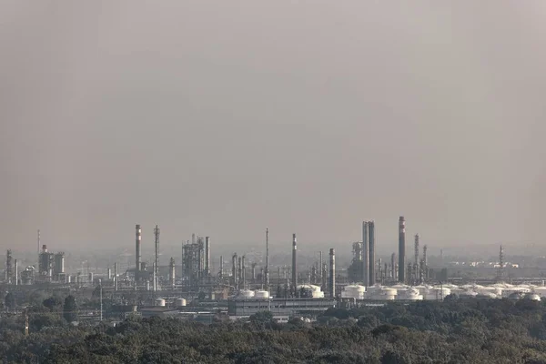 Oil refinery buildings with big silos and chimneys, dull weather with haze vibration in the air