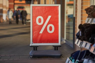 Large discount sign board on a shopping street showing just a percent sing in front of a shop entrance clipart