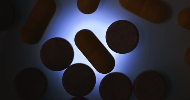 药物或药物丸在发亮的透明表面上旋转 背光昏暗 — 图库视频影像