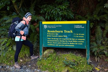 Fiordland, Yeni Zelanda - 17 Mart 2016: Routeburn Track patikasının danışma kurulunun önünde duran yürüyüşçü kız, Yeni Zelanda Güney Adası 'nda yürüyüş parkurunda büyük bir yürüyüşe başladı