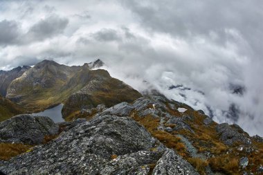 Routeburn Pisti 'ndeki yüksek dağ manzarası Yeni Zelanda Güney Adası' ndaki harika yürüyüş yolu sisli hava, uçurumlar ve göl.