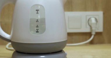 Electric kettle water heater at boiling point for hot beverages, plugged in on the kitchen counter